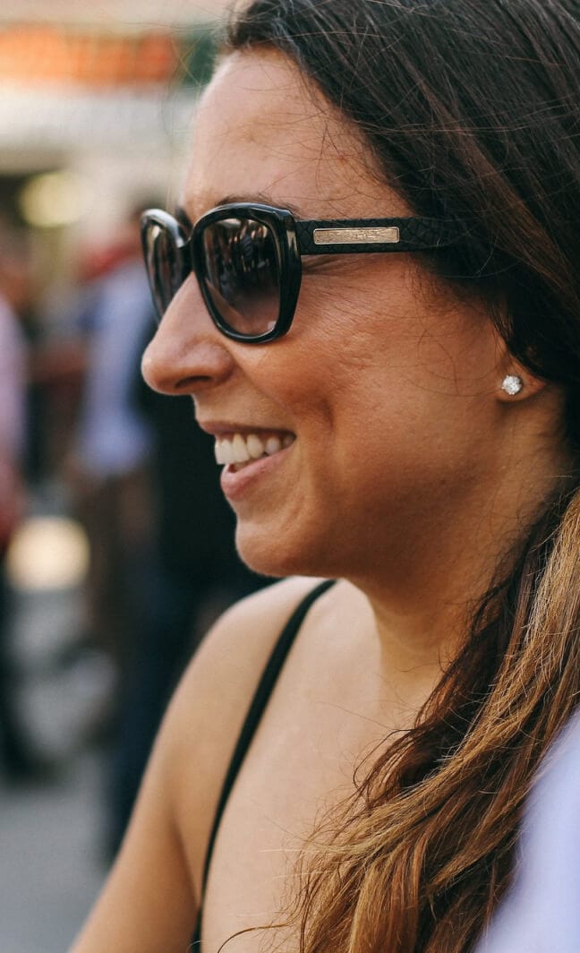 Profile of a person with sunglasses smiling warmly in a sunlit outdoor setting
