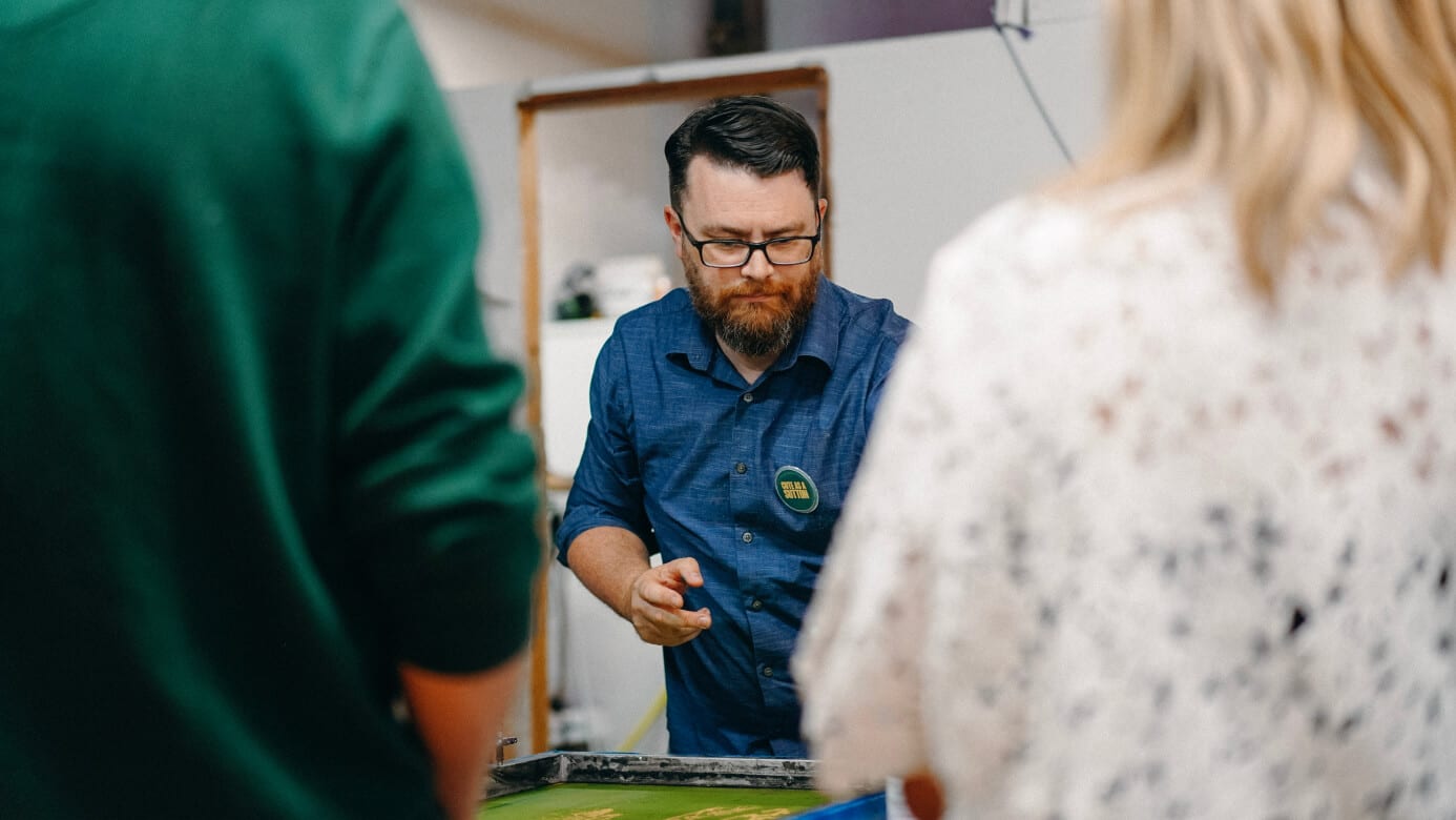 Person in a blue shirt attentively preparing a screen for printing, in a hands-on workshop setting