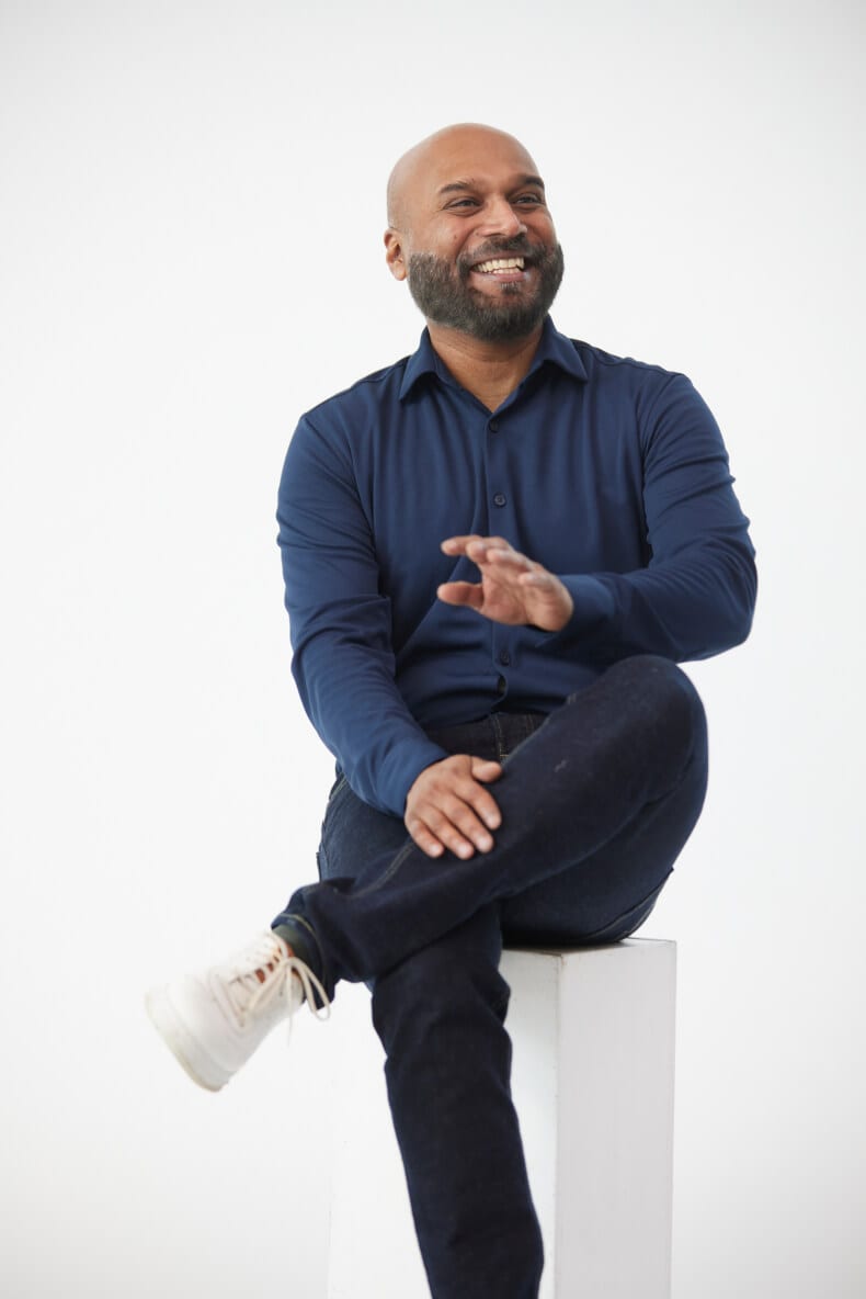 Person with a warm smile sitting atop a white pedestal with legs crossed