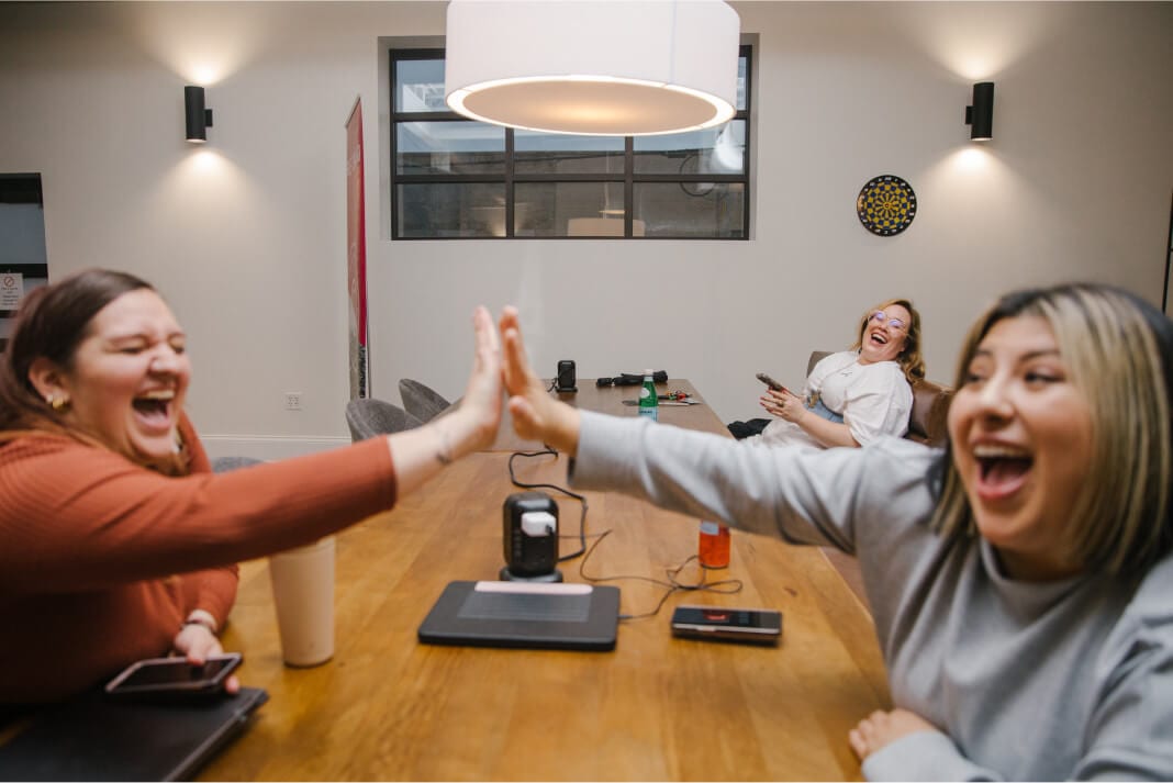 Two individuals giving each other a high five at a meeting table, showing joy and collaboration