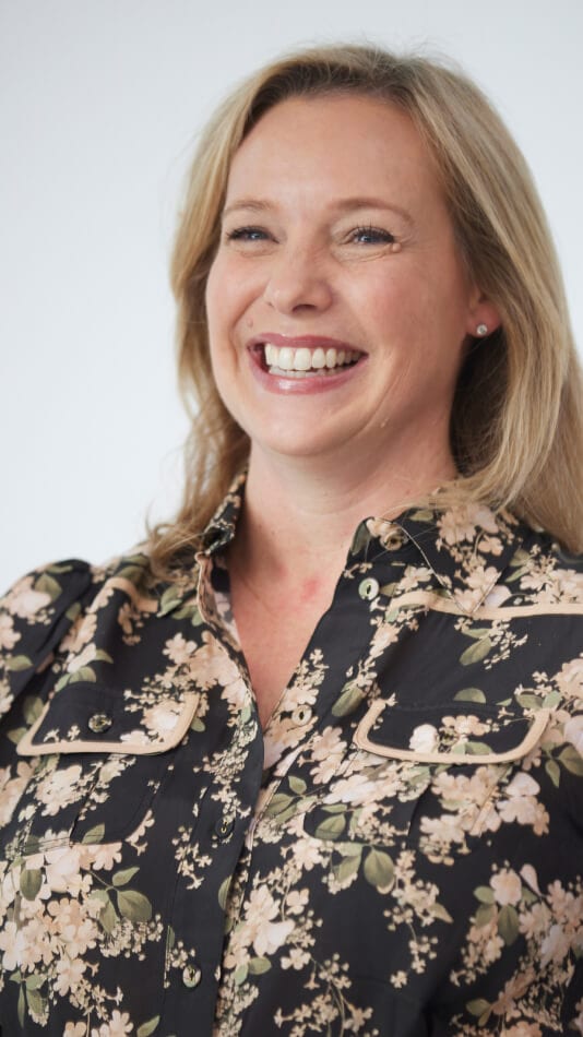 Headshot of a smiling person wearing a floral black blouse in a professional portrait
