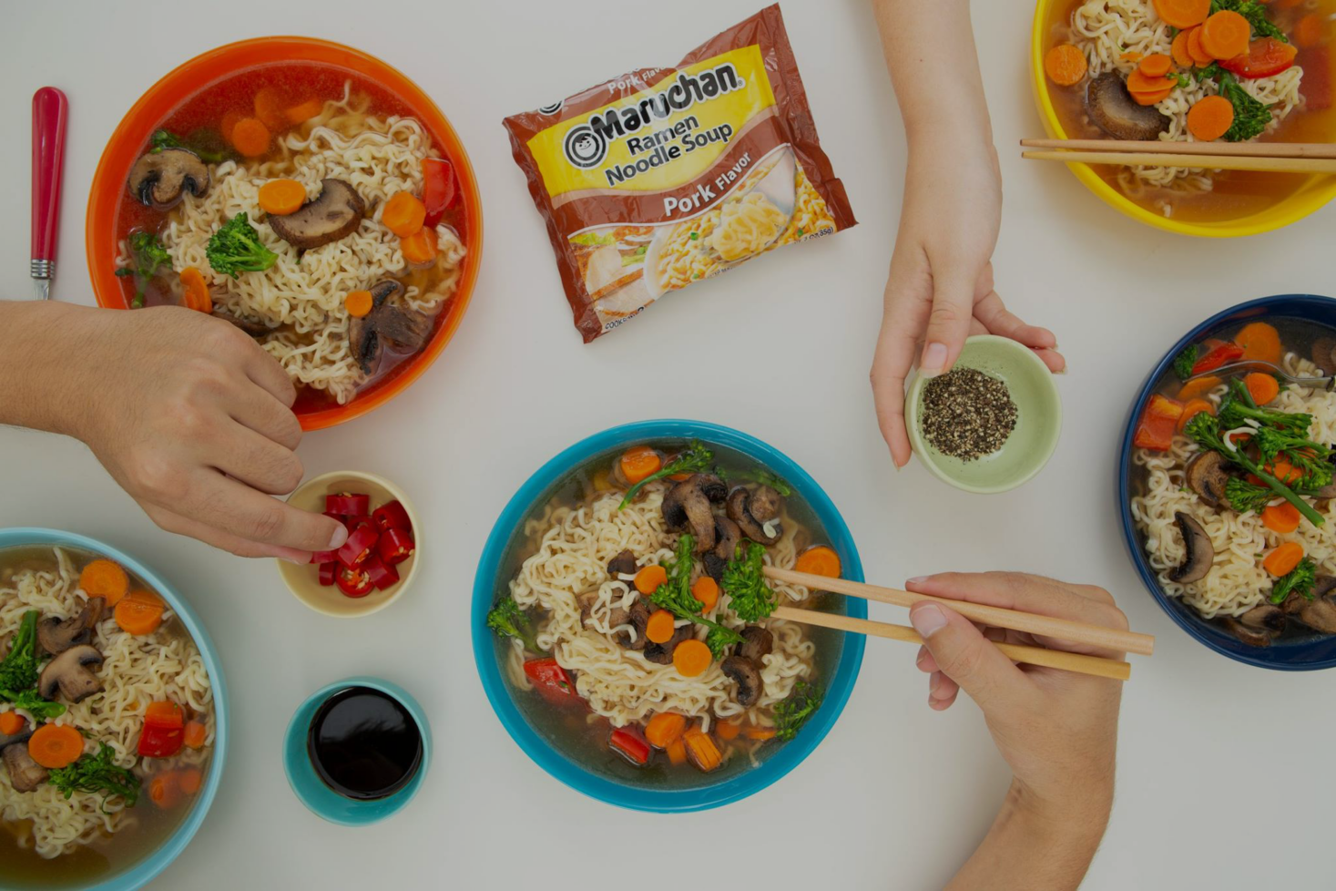 Hands preparing and serving instant ramen noodles with vegetables and pork flavor packet visible