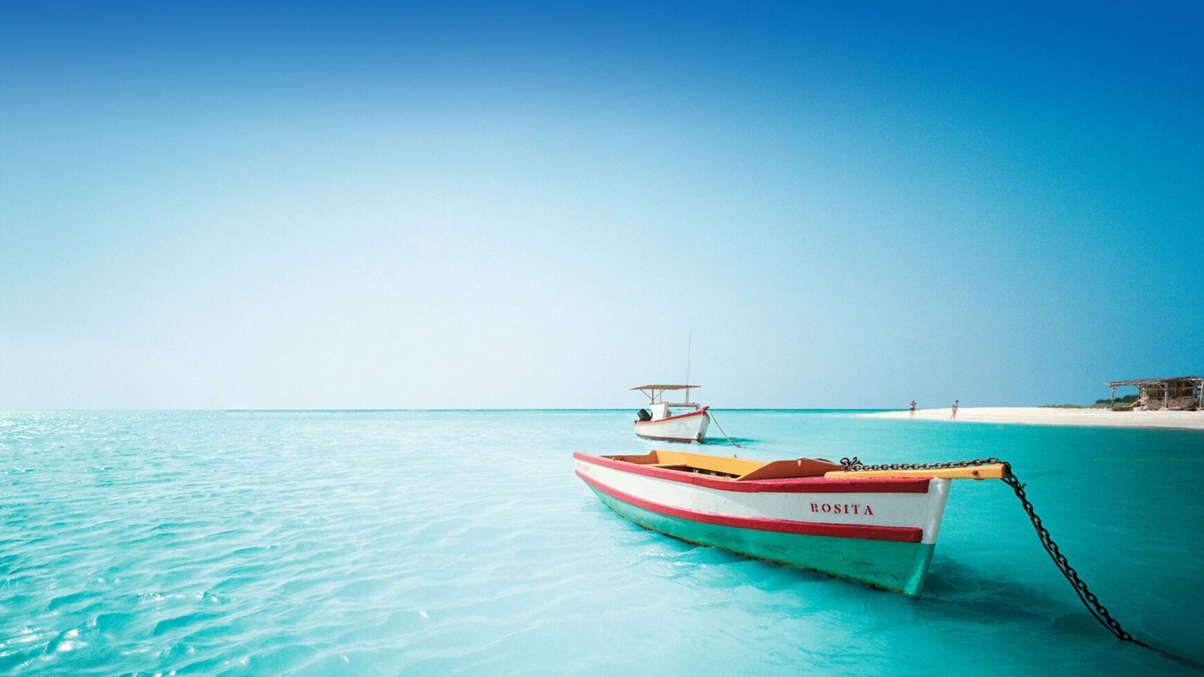 Serene tropical shoreline with clear blue water and a colorful boat in the foreground