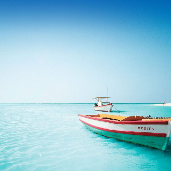 Serene tropical shoreline with clear blue water and a colorful boat in the foreground