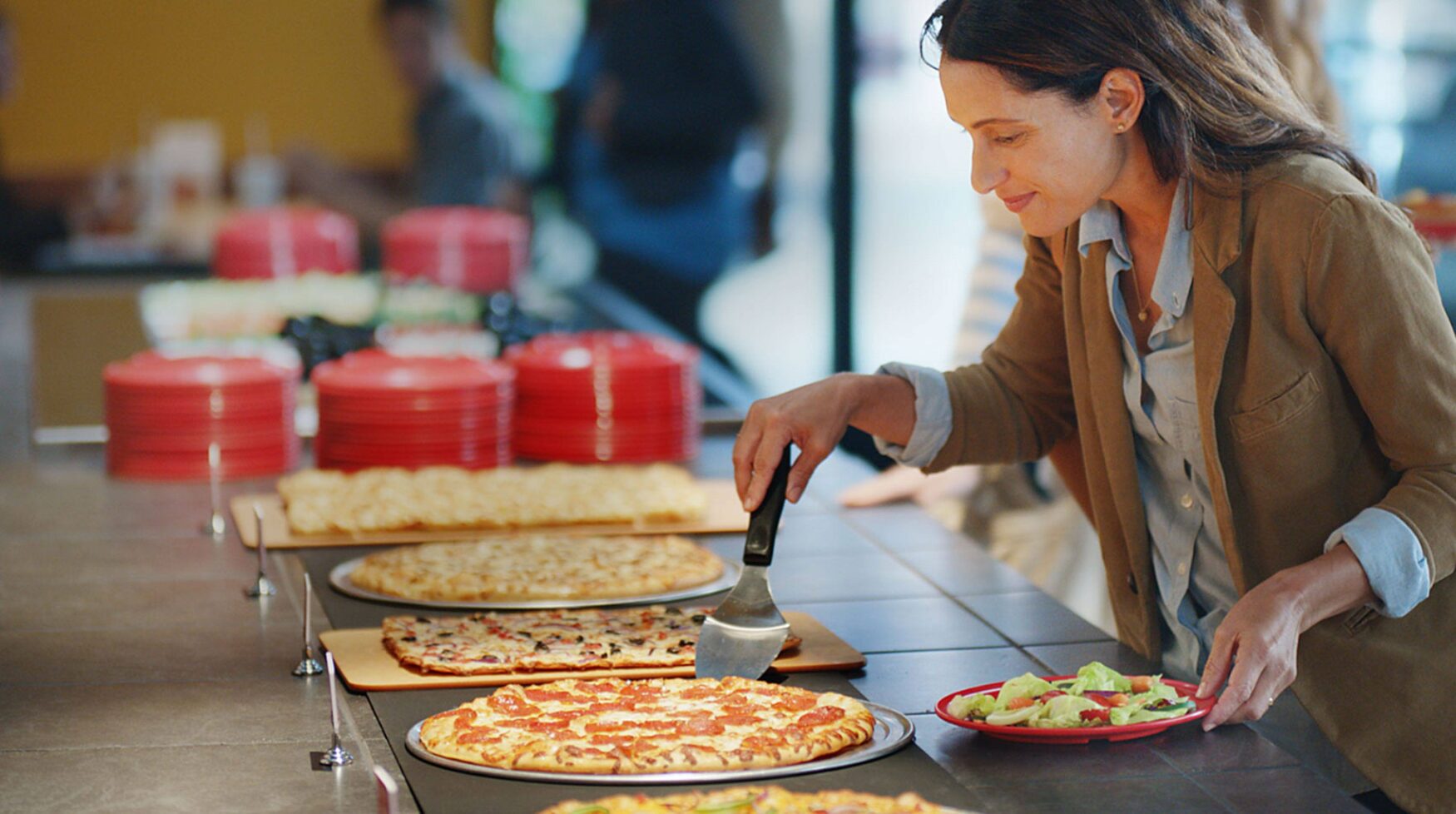 Customer grabbing a slice of pizza with a plate of salad in hand