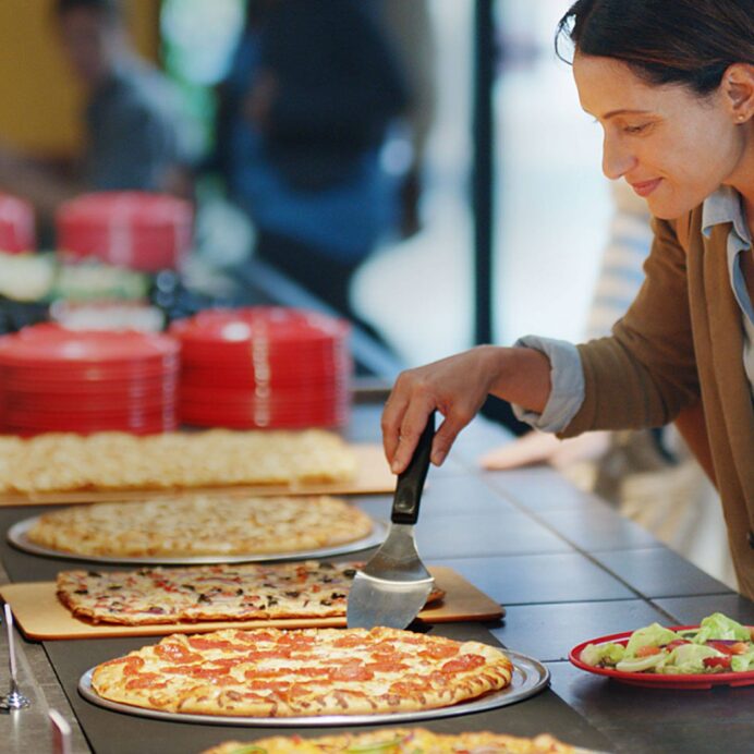 Customer grabbing a slice of pizza with a plate of salad in hand