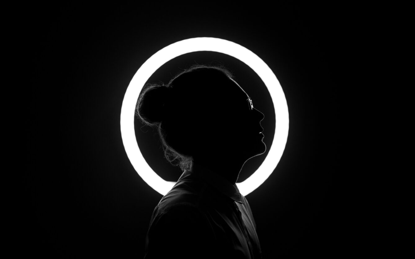 Silhouette of a person profiled against a circular light source creating a halo effect around their head.