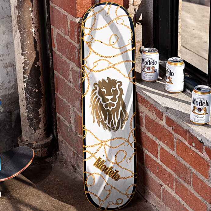 Modelo skateboard leaning up against a wall with cans of Modelo beside it