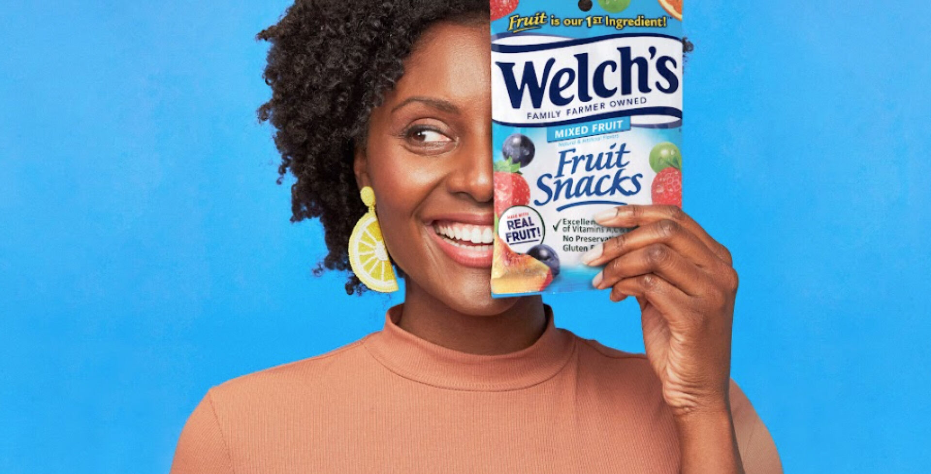 Woman smiling while holding a bag of Welch's fruit snacks in front of her face