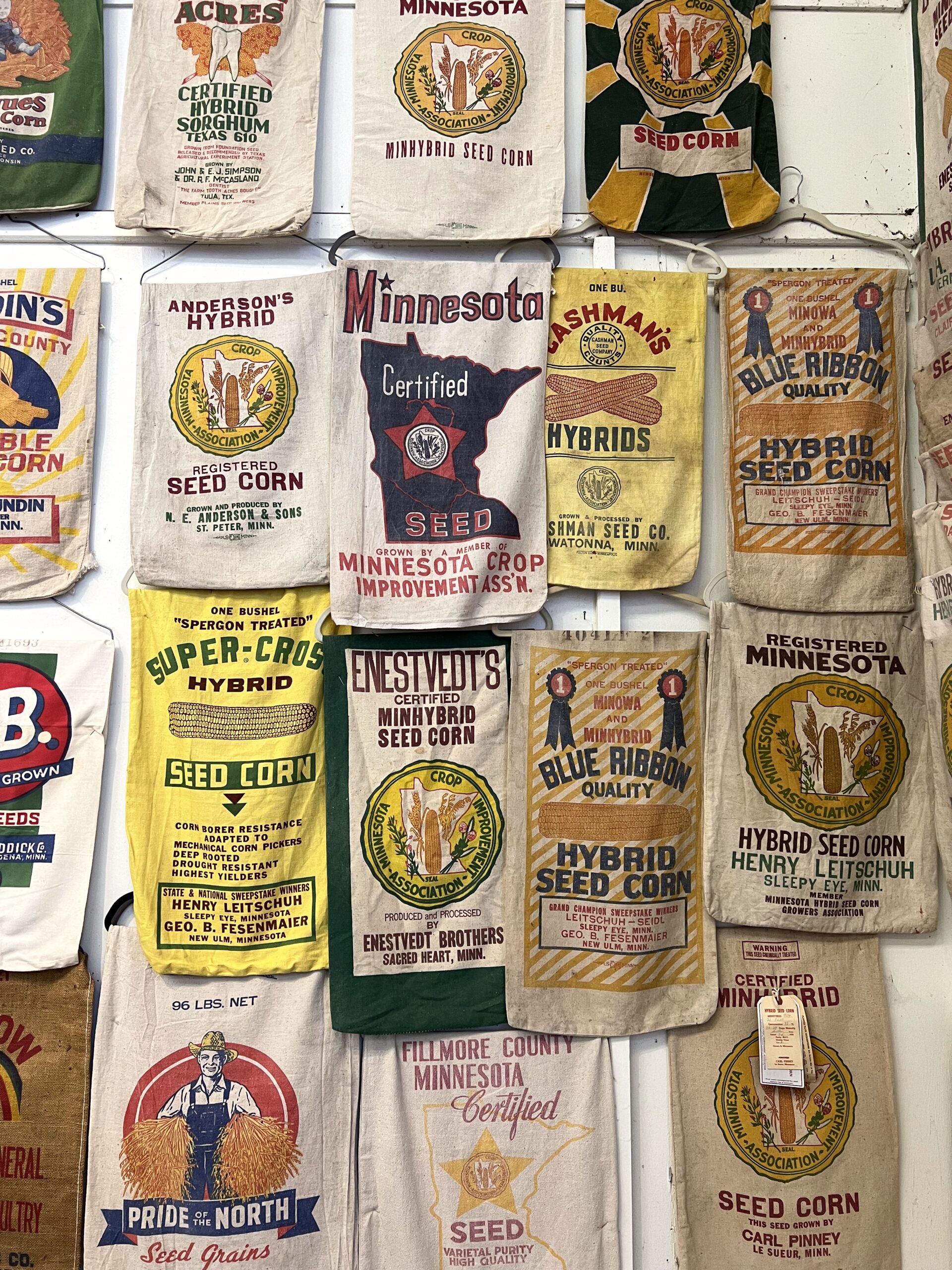 Vintage Minnesota seed corn sacks with colorful designs and logos displayed on a wall.