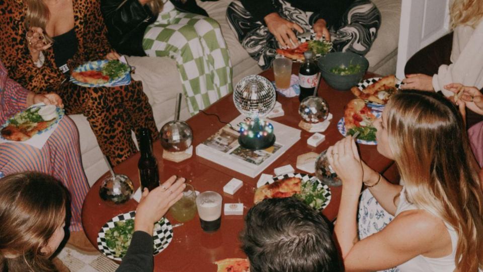A group of friends gathered around a coffee table eating and drinking