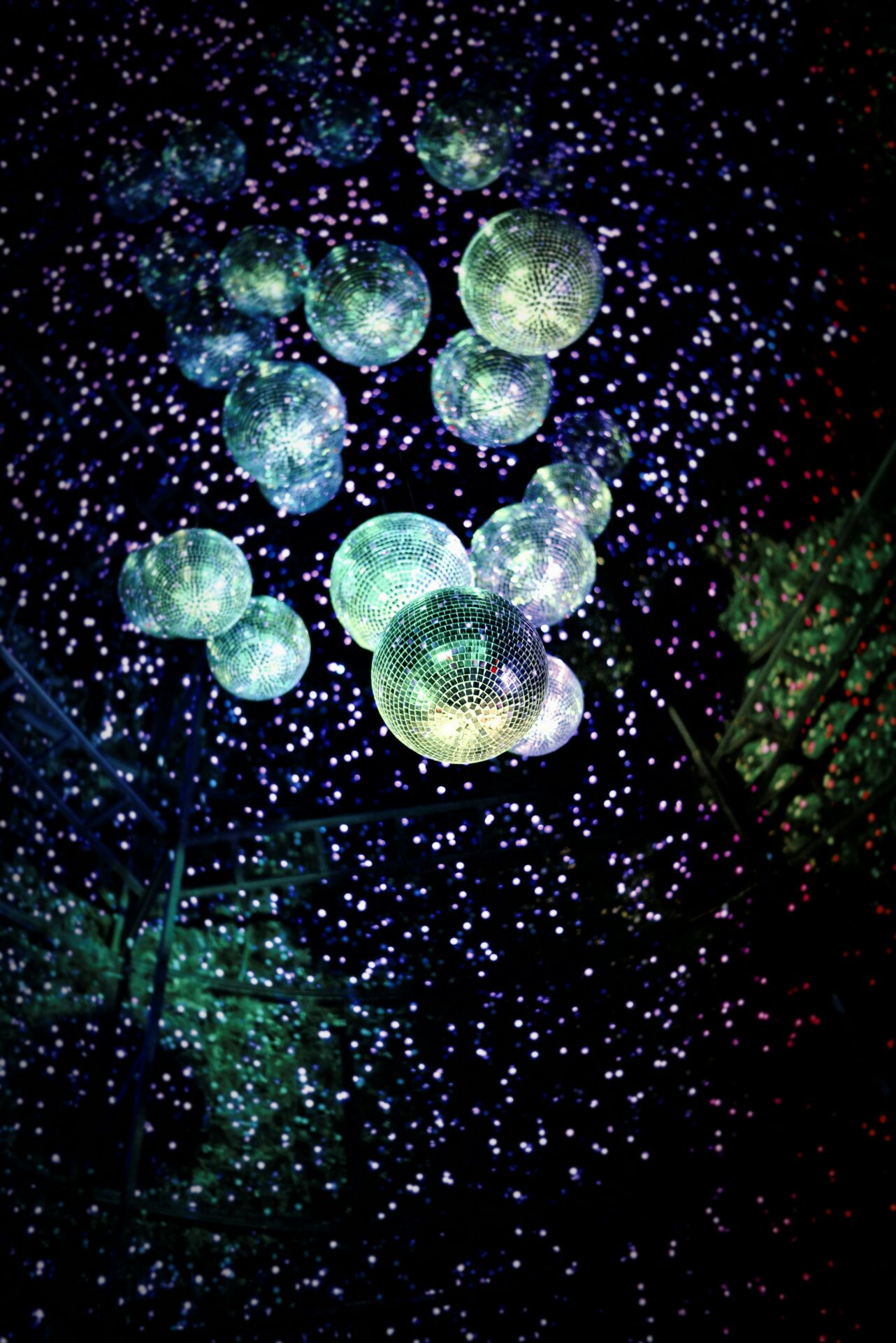 Image of disco balls hanging from the ceiling from below in a dark room with reflections of light scattered everywhere in the dark