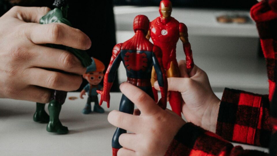 Close up image of a three super hero action figure toys, two in the hands of a small child and one in the larger hands of a grown man, presumably the child's father figure