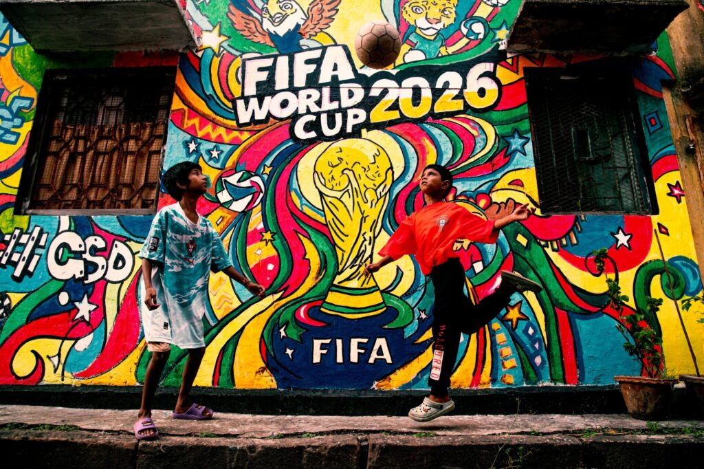 Two children play with a soccer ball in front of a brightly covered outdoor mural that says FIFA WORLD CUP