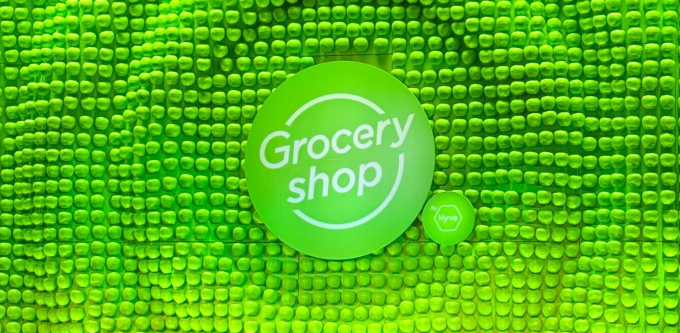 A stage background shows hundreds of lime green apples creating a wave-like texture with a sign in the foreground that says "Groceryshop"