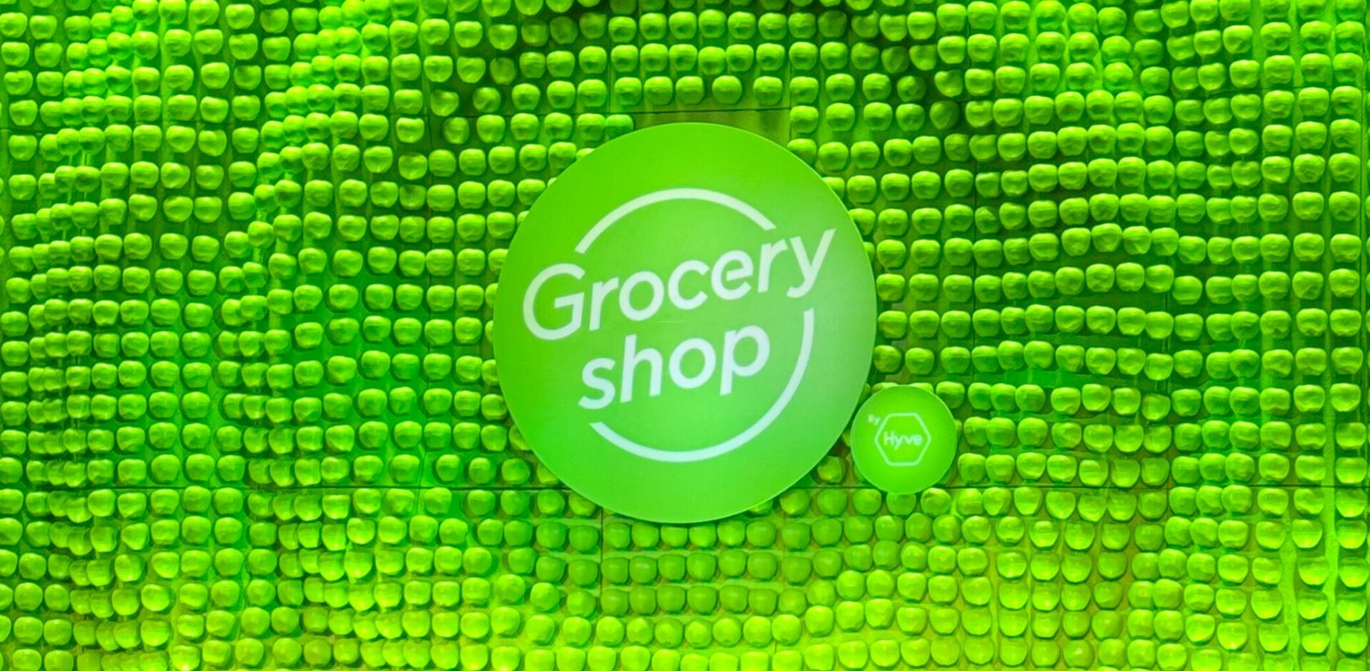 A stage background shows hundreds of lime green apples creating a wave-like texture with a sign in the foreground that says "Groceryshop"
